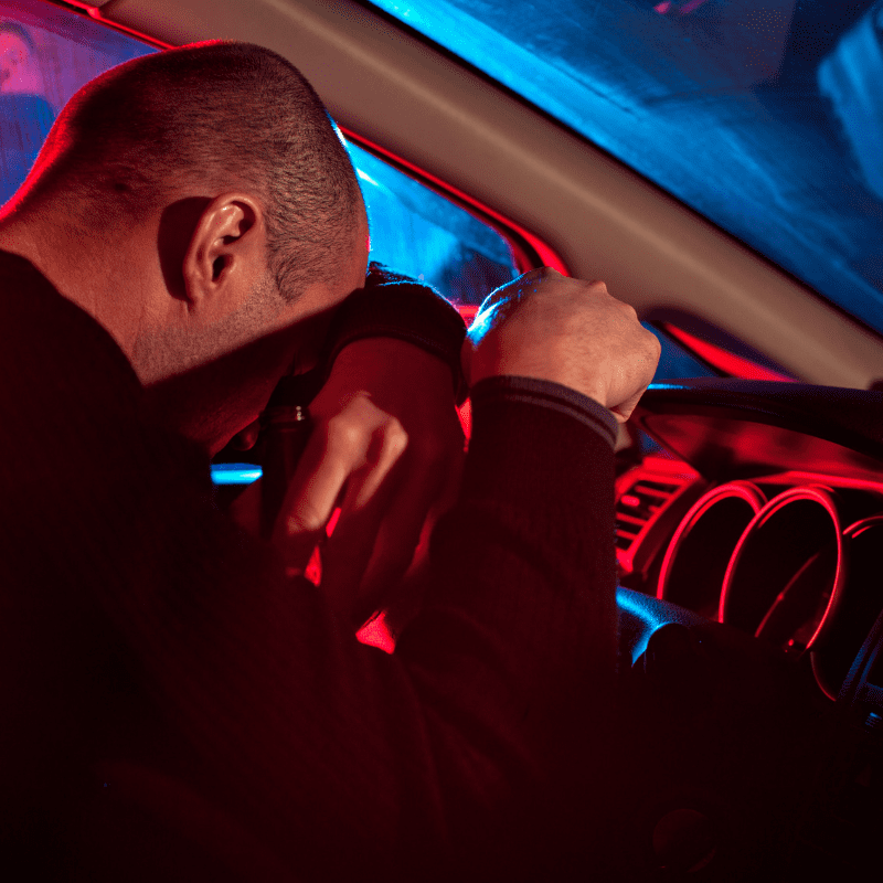 a drunk driver inside a car holding a bottle of beer