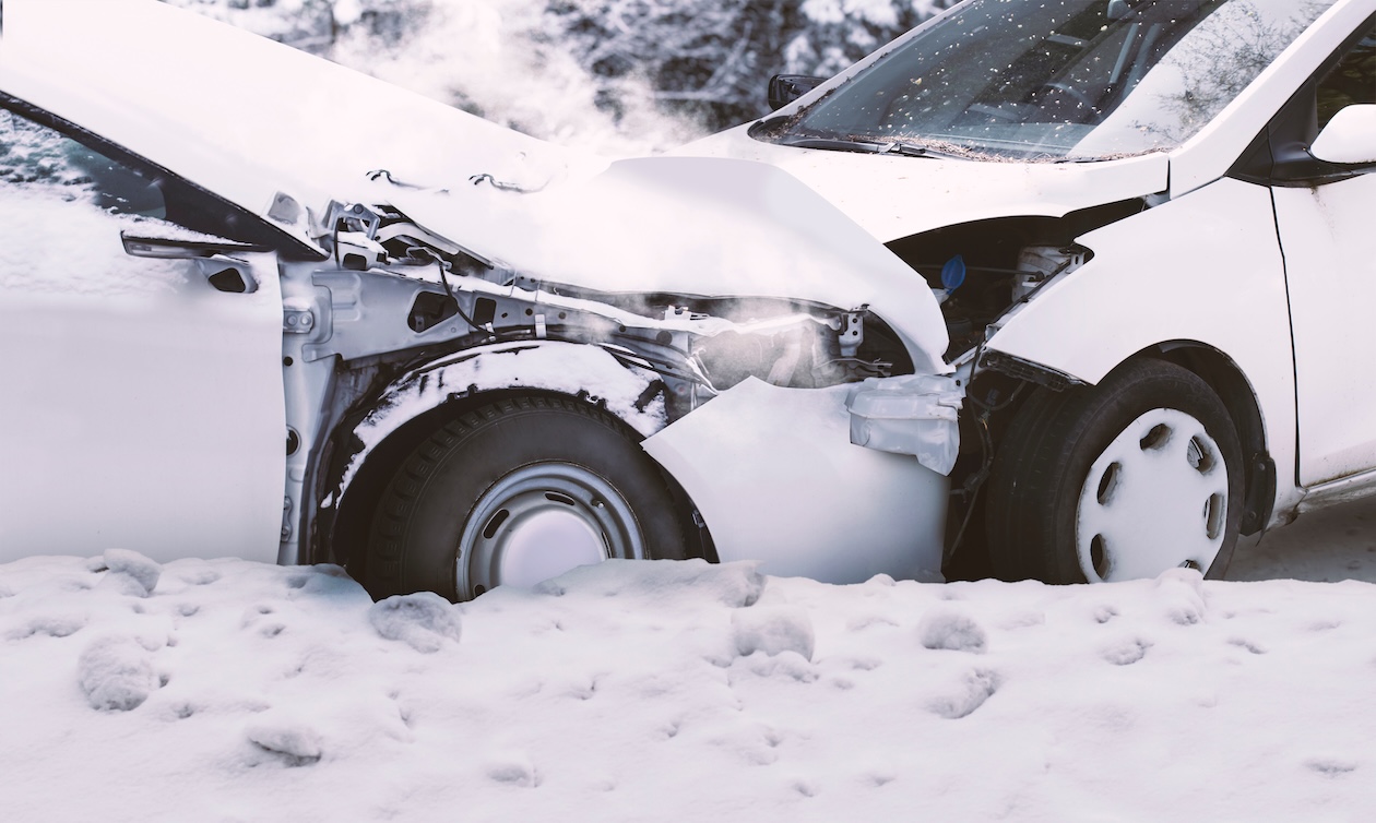 Two cars damaged in a front-end collision on a snowy road during winter conditions.