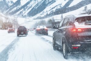 A snowy city highway with cars driving through heavy winter conditions on a slippery mountain road.