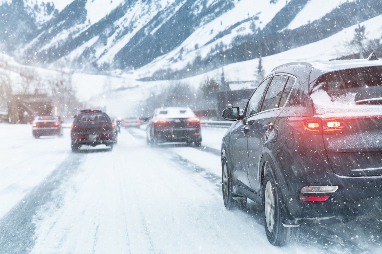A snowy city highway with cars driving through heavy winter conditions on a slippery mountain road.