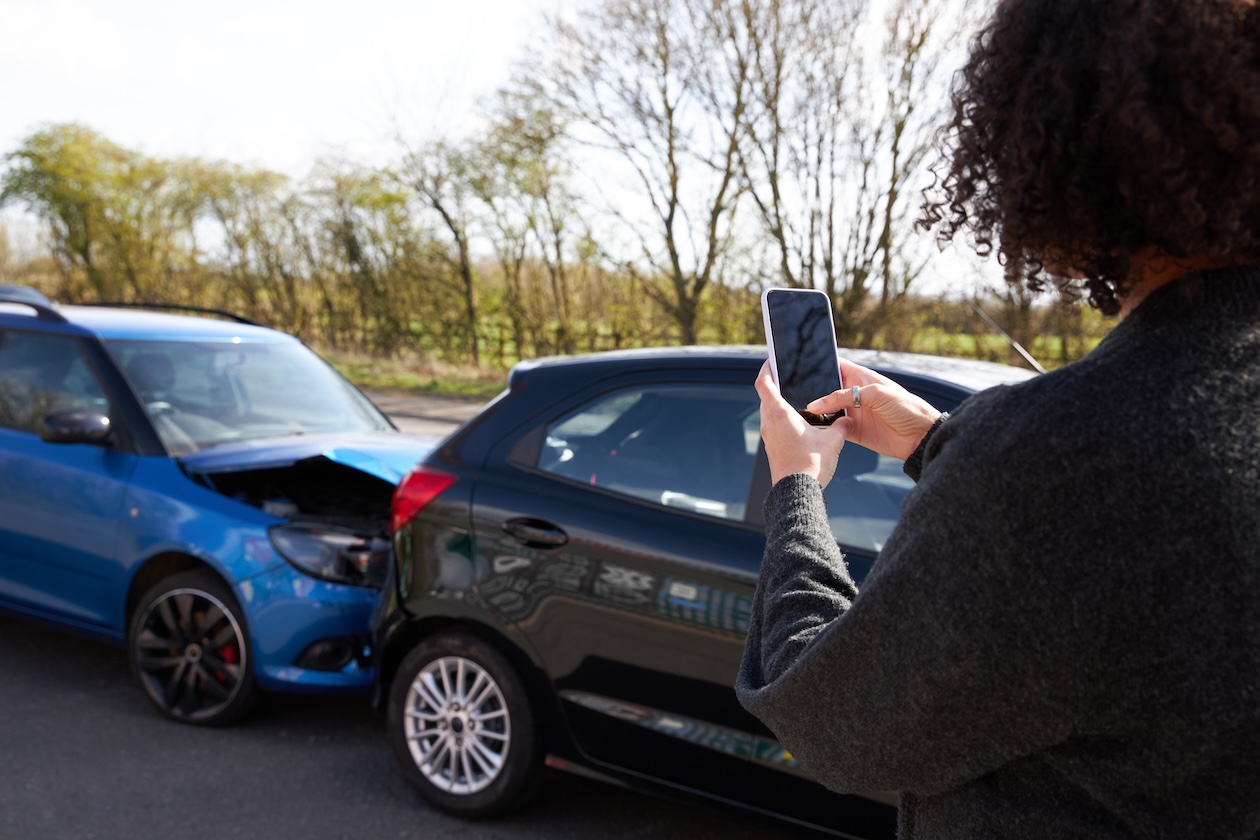 A woman photographing vehicle damage after a traffic accident to document the scene for an insurance claim.