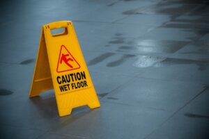 Yellow wet floor caution sign near a puddle of water, warning of a slippery surface in a public area