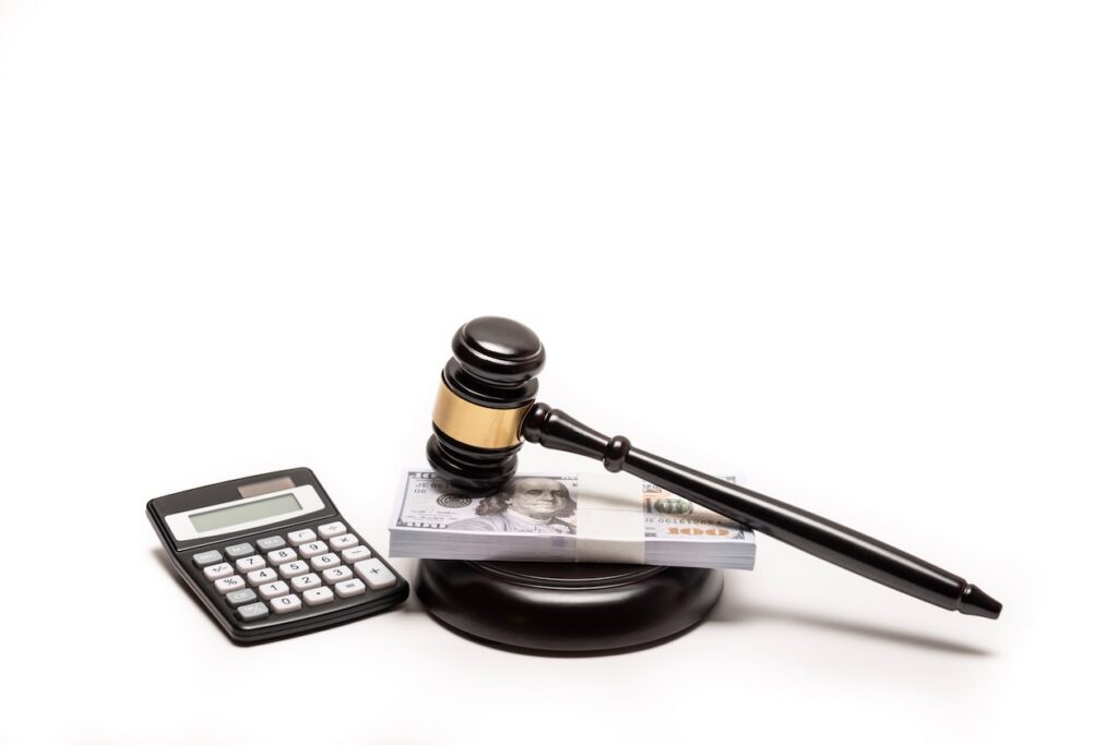 Judge’s gavel resting on a stack of cash beside a calculator, symbolizing legal fines, damages, bail, or financial judgments in a court case.