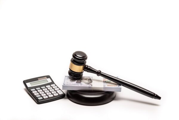 Judge’s gavel resting on a stack of cash beside a calculator, symbolizing legal fines, damages, bail, or financial judgments in a court case.