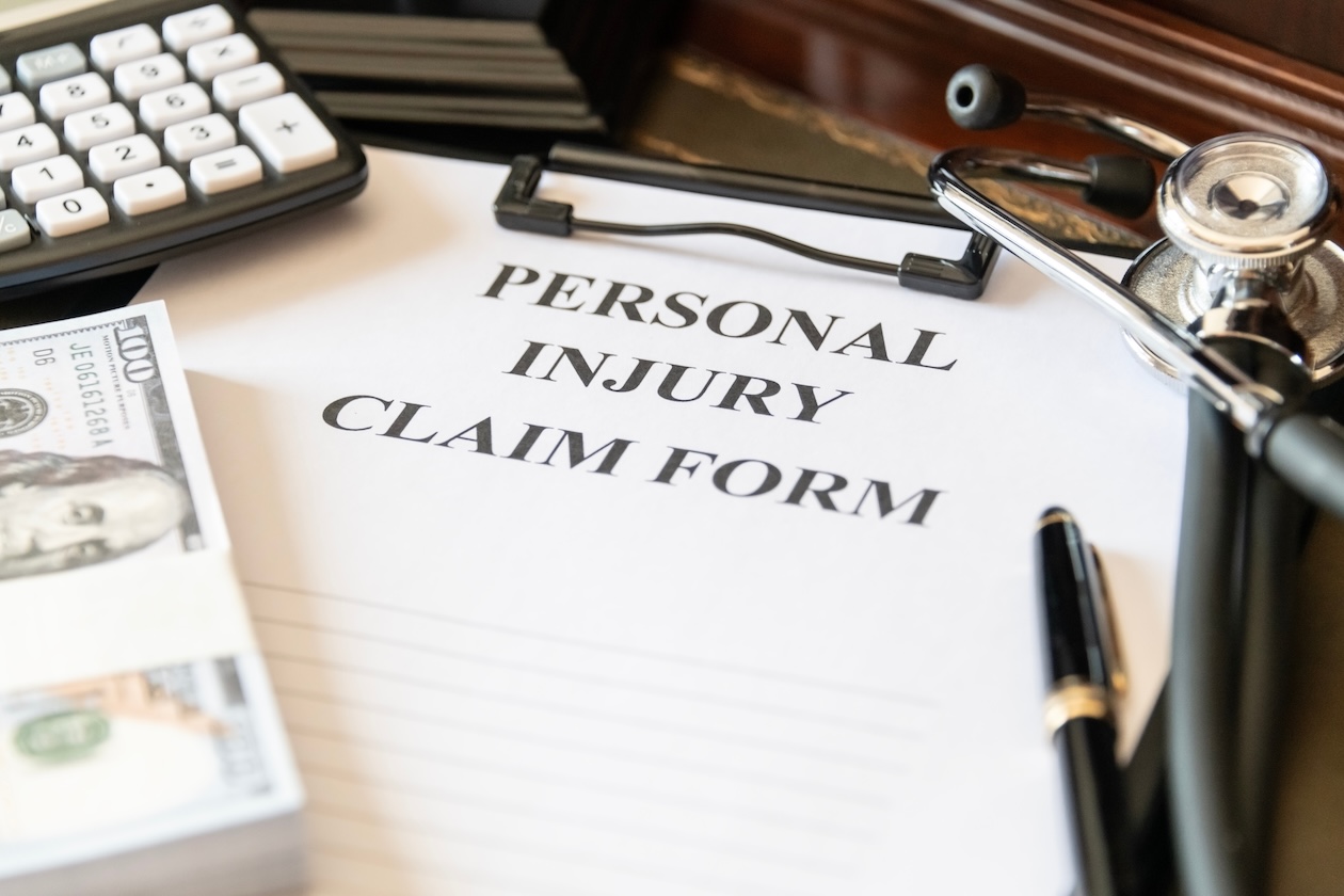 Close-up of a personal injury claim form with a stethoscope, calculator, and cash, representing medical expenses and financial damages in an injury case.
