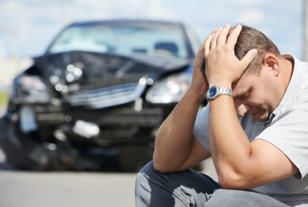 Upset driver sitting beside damaged car after a traffic accident in Nevada while speaking with insurance following a collision.