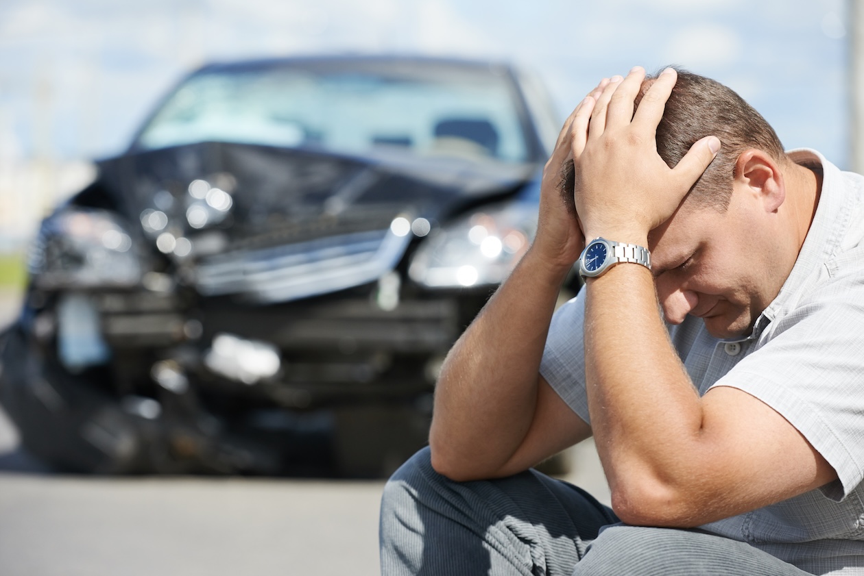 Upset driver sitting beside damaged car after a traffic accident in Nevada while speaking with insurance following a collision.